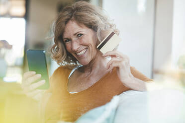 Happy mature woman sitting with credit card and smart phone - JOSEF15624