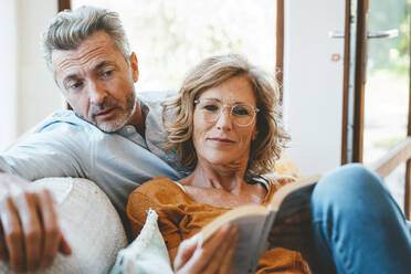 Reife Frau und Mann lesen gemeinsam zu Hause ein Buch - JOSEF15660