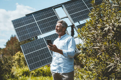 Älterer Mann mit Mobiltelefon vor Sonnenkollektoren stehend - JOSEF15664