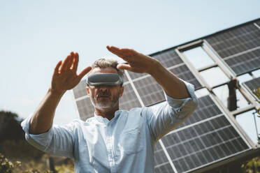 Älterer Mann gestikuliert mit einer futuristischen Brille vor Sonnenkollektoren - JOSEF15675