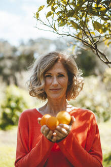 Lächelnde Frau hält Orangenfrüchte im Garten - JOSEF15689