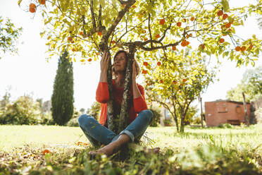 Glückliche reife Frau sitzt unter Orangenbaum im Garten - JOSEF15698