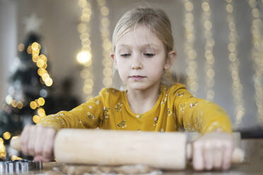 Blond girl rolling out dough on table at home - NJAF00079