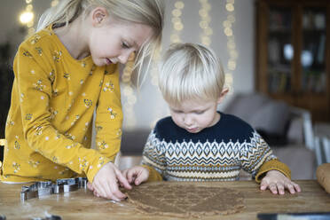 Blonder Bruder und blonde Schwester bereiten Kekse auf dem Tisch zu Hause vor - NJAF00087