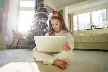 Mädchen mit langen Haaren, das einen Laptop benutzt und zu Hause auf dem Teppich sitzt - MDOF00383