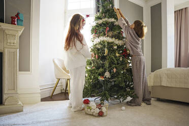 Geschwister schmücken den Weihnachtsbaum im Schlafzimmer zu Hause - MDOF00389