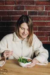 Smiling woman having salad with chopsticks in cafe - VSNF00206
