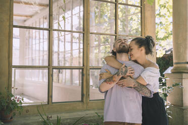 Affectionate woman embracing hipster boyfriend in front of window - NDEF00336