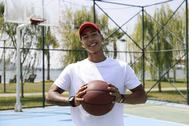 Lächelnder Mann hält Basketball auf einem Sportplatz - SYEF00023