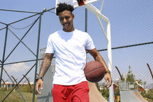 Glücklicher junger Mann mit Basketball auf dem Sportplatz - SYEF00027