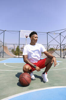 Junger Mann hockt beim Basketball auf dem Sportplatz - SYEF00029