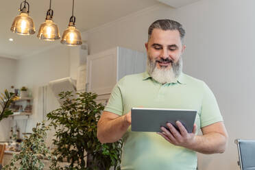 Smiling mature man using tablet PC with illuminated pendant lights in background at home - OSF01207