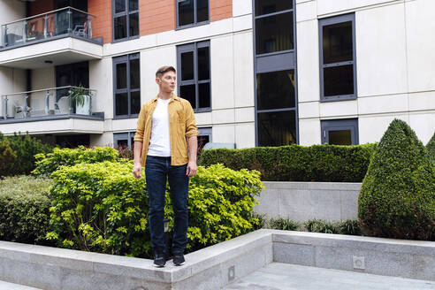 Junger Mann steht an einer Mauer vor einem Gebäude - ASGF03164