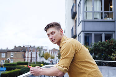 Handsome young man with smart phone leaning on railing - ASGF03168