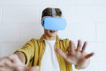 Young man gesturing wearing virtual reality headset in front of white wall - ASGF03177