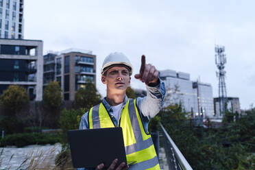 Engineer wearing hardhat pointing and holding laptop - ASGF03181