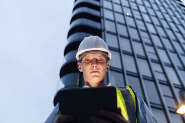 Engineer using tablet PC in front of building at dusk - ASGF03186