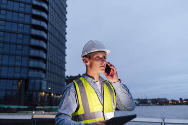 Ingenieur mit Tablet-PC, der in der Abenddämmerung mit seinem Smartphone telefoniert - ASGF03191