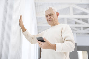 Rentner mit Smartphone berührt Heizkörper zu Hause - EYAF02371