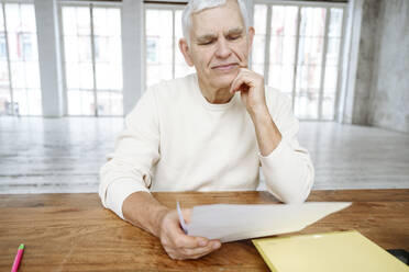 Älterer Mann mit Hand am Kinn, der zu Hause finanzielle Rechnungen liest - EYAF02378