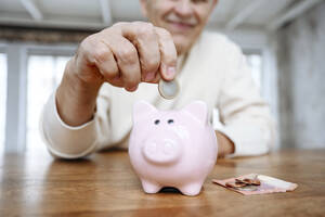 Man putting coin into piggy bank at home - EYAF02384