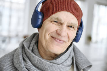 Glücklicher Mann mit Strickmütze, der über Kopfhörer Musik hört - EYAF02395