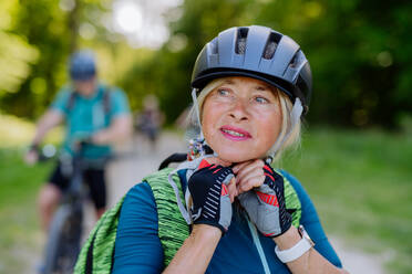 Ein aktives Seniorenpaar fährt im Sommer im Park Fahrrad, die Frau setzt den Helm auf, Konzept der gesunden Lebensweise. - HPIF03510