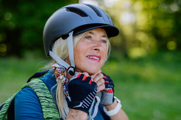 Ein aktives Seniorenpaar fährt im Sommer im Park Fahrrad, die Frau setzt den Helm auf, Konzept der gesunden Lebensweise. - HPIF03511