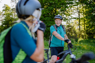 Ein aktives Seniorenpaar fährt im Sommer im Park Fahrrad, die Frau setzt den Helm auf, Konzept der gesunden Lebensweise. - HPIF03514