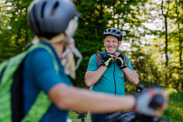 Ein aktives älteres Paar fährt mit dem Fahrrad im Sommerpark, der Mann setzt den Helm auf, gesunder Lebensstil Konzept. - HPIF03515
