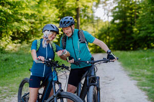 Ein Porträt eines aktiven Seniorenpaares, das im Sommer im Park Fahrrad fährt und auf seine Sport-Smartwatch schaut, um seine Leistung zu überprüfen. - HPIF03516