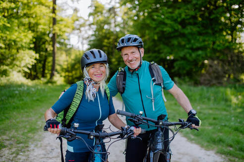 A portrait of active senior couple riding bicycles at summer park, standing on path and looking at camera - HPIF03517