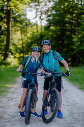 Porträt eines aktiven älteren Paares, das im Sommer im Park Fahrrad fährt, auf dem Weg steht und in die Kamera schaut - HPIF03519