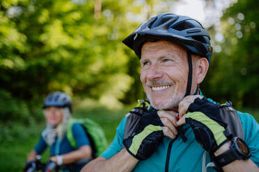 AN Active senior couple riding bicycles at summer park, man is putting on helmet, healthy lifestyle concept. - HPIF03521