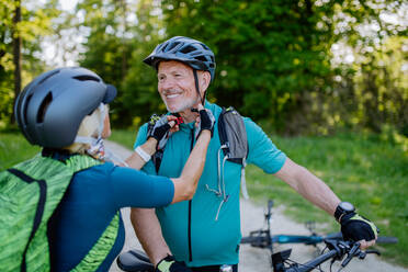 Ein aktives Seniorenpaar fährt im Sommer im Park Fahrrad, setzt einen Helm auf, Konzept der gesunden Lebensweise. - HPIF03526