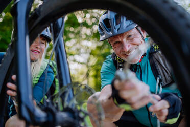 Ein aktives Seniorenpaar repariert ein Fahrrad und pumpt im Sommer in der Natur Reifen auf. - HPIF03530