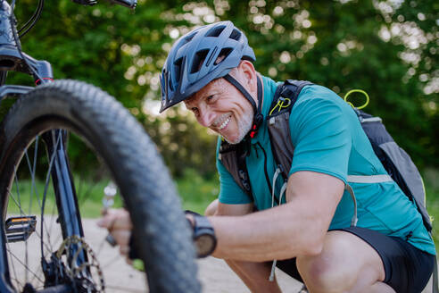 An active senior man repairing bicycle, pumping up tire in nature in summer. - HPIF03531