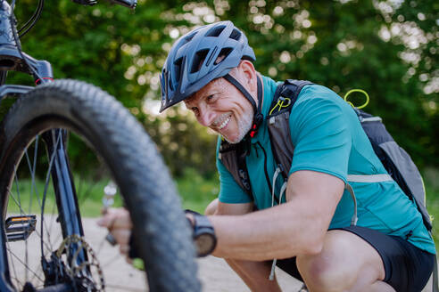 Ein aktiver älterer Mann repariert ein Fahrrad und pumpt im Sommer in der Natur Reifen auf. - HPIF03531