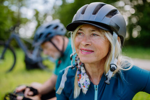 An active senior couple riding bicycles at summer park, woman with bicycle helmet, healthy lifestyle concept. - HPIF03540