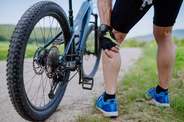 Nahaufnahme eines aktiven älteren Mannes in Sportkleidung, der nach dem Radfahren in einem Park im Sommer unter Schmerzen im Knie leidet. - HPIF03548