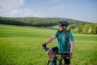 An active senior man with electric bicycles on meadow in summer, healthy lifestyle concept. - HPIF03553