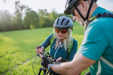 Ein aktives Seniorenpaar ruht sich nach einer Fahrradtour im Sommerpark aus und benutzt sein Smartphone. - HPIF03554