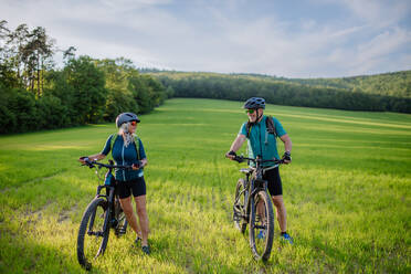 Ein aktives Seniorenpaar mit Elektrofahrrädern auf einer Wiese im Sommer, Konzept des gesunden Lebensstils. - HPIF03560