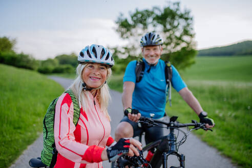 An ctive senior couple riding electric bicycles on road at summer park, healthy lifestyle concept. - HPIF03572