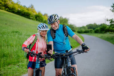 Ein aktives Seniorenpaar ruht sich nach einer Fahrradtour im Sommerpark aus und benutzt sein Smartphone. - HPIF03573