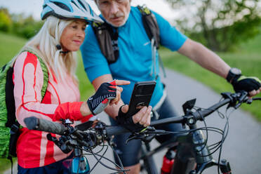 Ein aktives Seniorenpaar ruht sich nach einer Fahrradtour im Sommerpark aus und benutzt sein Smartphone. - HPIF03574