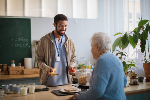 Eine junge Pflegerin serviert einer älteren Frau im Pflegeheim das Frühstück. - HPIF03593