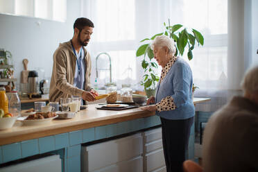 Eine junge Pflegerin serviert einer älteren Frau im Pflegeheim das Frühstück. - HPIF03595