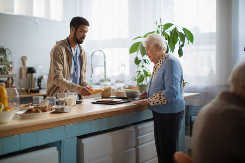 A young caregiver serving breakfast to elderly woman in nursing home care center. - HPIF03595