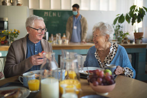 Eine lächelnde ältere Frau und ein Mann genießen das Frühstück in einem Pflegeheim. - HPIF03617
